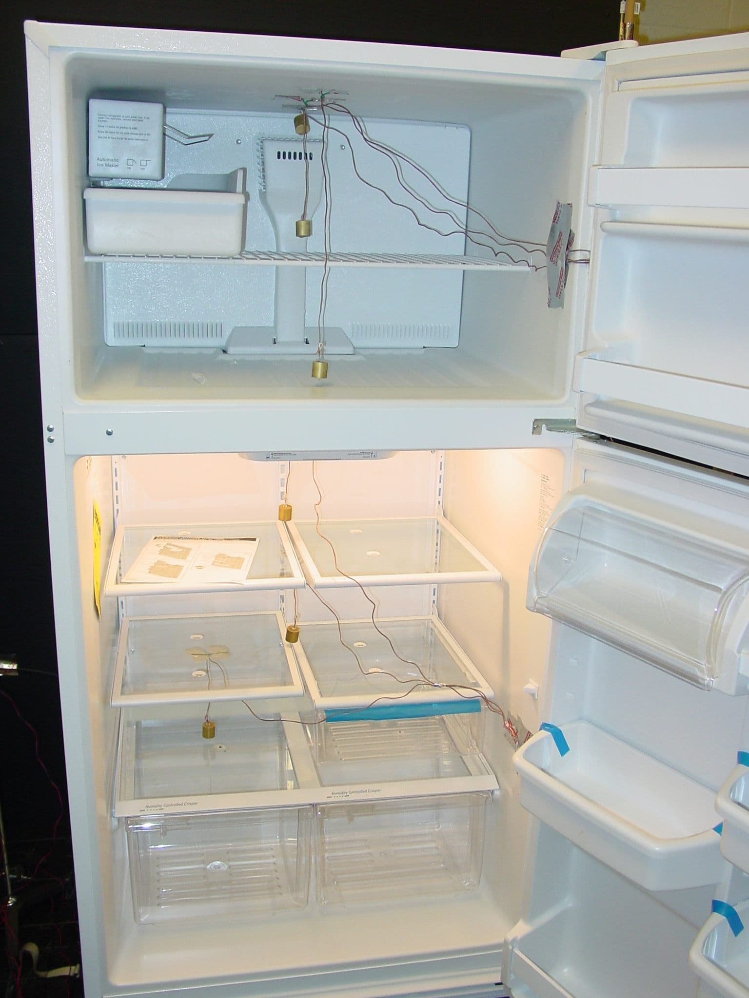 An empty open refrigerator with its shelves and door bins ready for cleaning